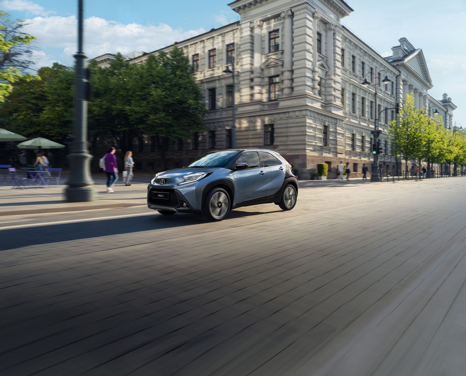 Aygo X drives sunny city streets with its canvas roof open. 